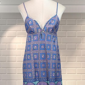 May include: A long, blue dress with a geometric and floral pattern. The dress features thin straps, a V-neckline with lace trim, and a flowing skirt. The color palette includes shades of blue, purple, and teal.