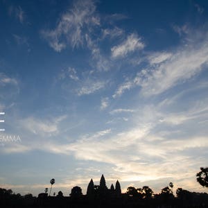 Op de afbeelding: Silhouet van een tempelcomplex tegen een blauwe lucht met witte wolken. De lucht is lichtblauw met witte wolken. De tempel is een donker silhouet tegen de lucht.