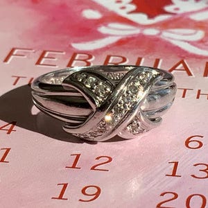 Può includere: Un anello d'argento con un design a croce e piccoli diamanti incastonati nella fascia.