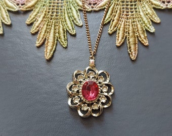 May include: A gold necklace with a pink rhinestone flower pendant.