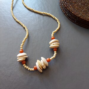 May include: A beige necklace with orange beads and white shell-shaped pendants.