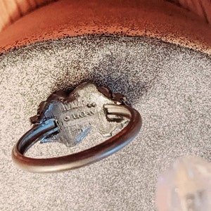 May include: A silver-toned metal ring featuring a thin, circular band and a textured, raised centerpiece. The underside of the centerpiece displays the stamped text "AVON" with a copyright symbol, indicating the manufacturer of this jewelry piece.