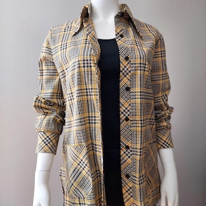 Peut inclure: Une chemise à carreaux jaune, noir et blanc, avec un col et deux poches avant. La chemise est ouverte, révélant un haut noir en dessous. Les manches sont retroussées. La chemise est présentée sur un mannequin.