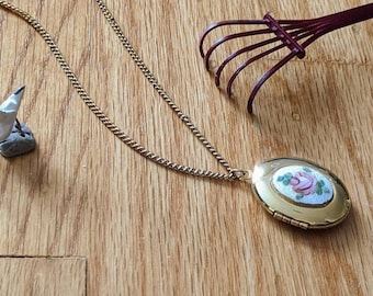 May include: A gold chain necklace with a gold locket pendant. The locket has a white enamel background with a pink rose painted on it.