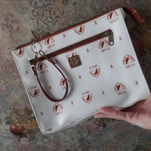 May include: White leather clutch with a brown zipper and a brown wrist strap. The clutch has a repeating pattern of a red crest with the word "Gitano" printed on it.
