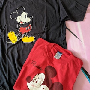 以下が含まれることがあります： ミッキーマウスがプリントされたTシャツ2枚。上のTシャツは黒地に白のミッキーマウスのプリント。下のTシャツは赤地に白のミッキーマウスのプリントで、前面に「フロリダ」の文字がプリントされている。