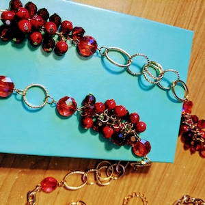 May include: A red and gold necklace with multiple strands of red beads and gold chain links. The necklace is displayed on a turquoise blue box.