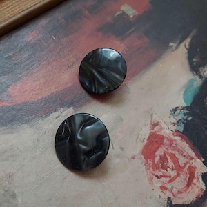 May include: A pair of black round earrings with a marbled pattern.