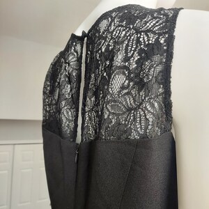 May include: A black dress with a lace overlay on the shoulders and upper back. The dress has a sleeveless design and a zipper closure. The lace detailing adds a touch of elegance to the garment.