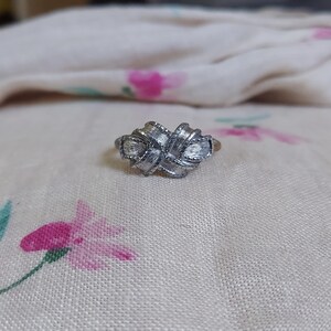 May include: A silver-toned metal ring featuring a central knot design with a textured, brushed finish. The knot is composed of interwoven bands that create a layered, dimensional appearance across the front of the ring band.