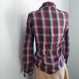 May include: A long-sleeved plaid shirt in a red, black, and light blue pattern. The shirt is displayed on a mannequin, showcasing the back of the garment. The plaid design is a classic style, suitable for casual wear.