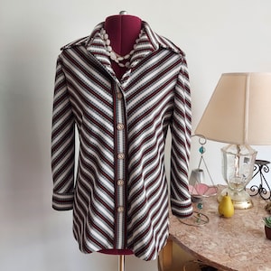 May include: A long-sleeved, striped shirt with a button-down front and a collar. The shirt is black and white with diagonal stripes. The shirt is on a mannequin.