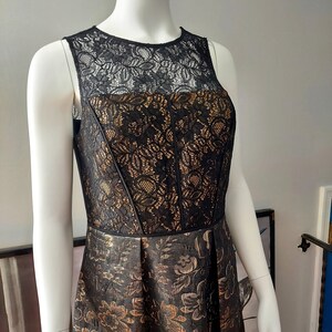 May include: A sleeveless black and gold dress on a mannequin. The bodice features black lace over a gold fabric, with a fitted design. The skirt is a darker gold with a floral pattern. The dress is designed for formal occasions.