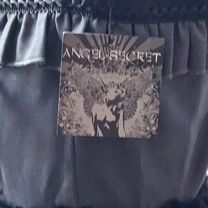 Op de afbeelding: Een zwarte rok met een gerimpelde tailleband en een zwart-wit label met de tekst "Angel Secret".