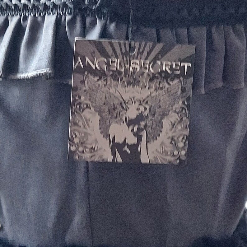 Op de afbeelding: Een zwarte rok met een gerimpelde tailleband en een zwart-wit label met de tekst "Angel Secret".
