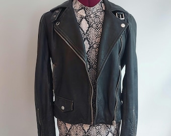May include: Black leather jacket with a classic asymmetrical zipper closure, lapel collar, and zippered sleeves. The jacket is displayed on a mannequin with a snakeskin print top underneath. The jacket has a small pocket on the front.