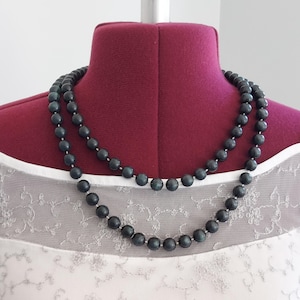 Puede incluir: Un collar de doble cadena hecho de cuentas de color verde oscuro. El collar se muestra en un maniquí.