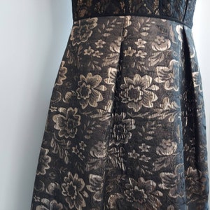 May include: A black dress with a floral pattern in gold and silver. The bodice features a black lace design, and the skirt is pleated. The dress is suitable for formal events.