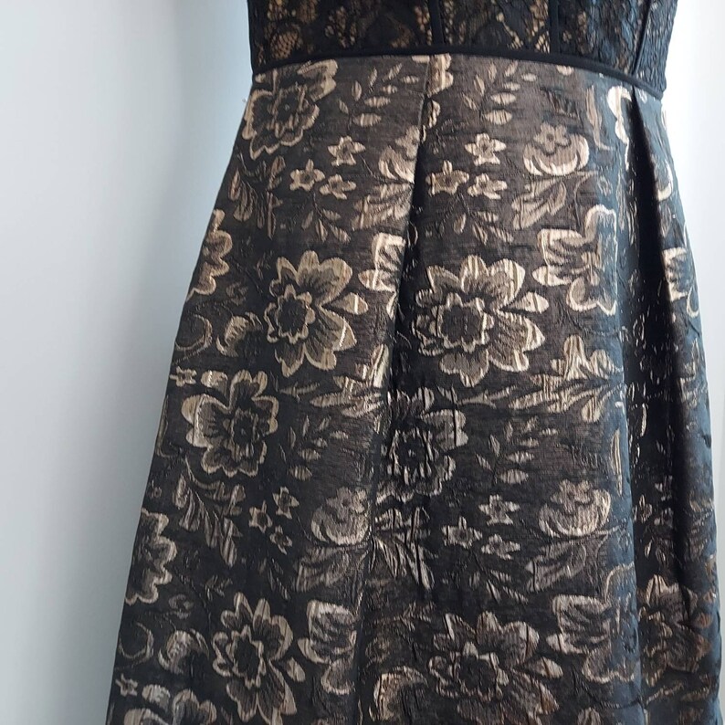 May include: A black dress with a floral pattern in gold and silver. The bodice features a black lace design, and the skirt is pleated. The dress is suitable for formal events.