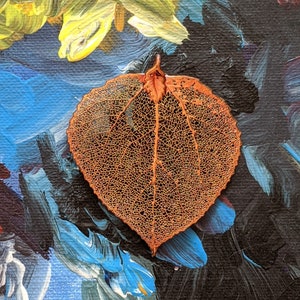May include: A delicate, dried leaf with an intricate network of veins, displayed against a colourful abstract background of blue, yellow, and black paint.