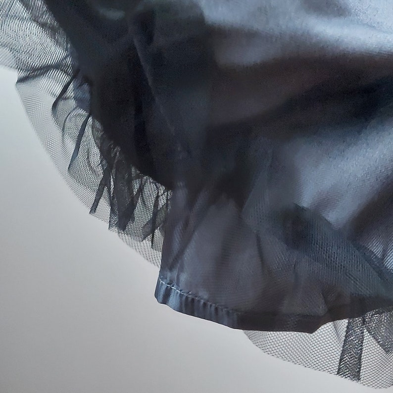 Op de afbeelding: Een zwarte tule rok met een satijnen tailleband. De rok is geplooid bij de taille en heeft een gerimpelde zoom.