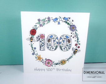 Puede incluir: Una tarjeta blanca con una corona de flores que rodea el número 100. La corona está hecha de flores coloridas, hojas y abejas. El texto "Happy 100th Birthday" está escrito debajo de la corona. El texto "DIMENSIONAL ART" está escrito en la esquina inferior derecha.