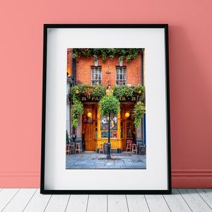 May include: A vintage-style pub with a green awning and the words "21  PARR - 21" above the entrance. The pub has two large windows with yellow frames and a wooden door. There are hanging plants and flowers in front of the pub.