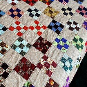 May include: A quilt made of various patterned fabric squares sewn together in a checkerboard pattern. The squares are in a variety of colors, including red, green, blue, purple, and brown. The quilt is made of a light brown fabric.