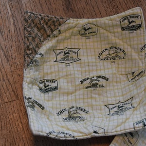 May include: A set of two yellow and white fabric pot holders with a repeating pattern of the John Deere logo and the text "John Deere Molin Ill".