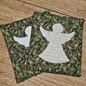 May include: Two green and black fabric coasters with a white angel design. The angel has a handwritten message that says "Merry Christmas" and "Happy Holidays".