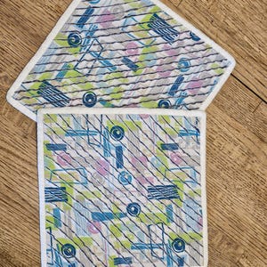 May include: Two white-trimmed kitchen pot holders with a geometric pattern in shades of blue, green, and pink.
