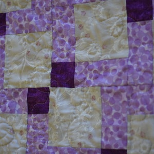 May include: A quilt made of purple and cream fabric squares. The purple squares have a pattern of small white dots. The cream squares have a floral pattern.