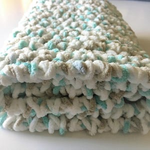 May include: A soft, crocheted baby blanket in white, beige, and light blue.