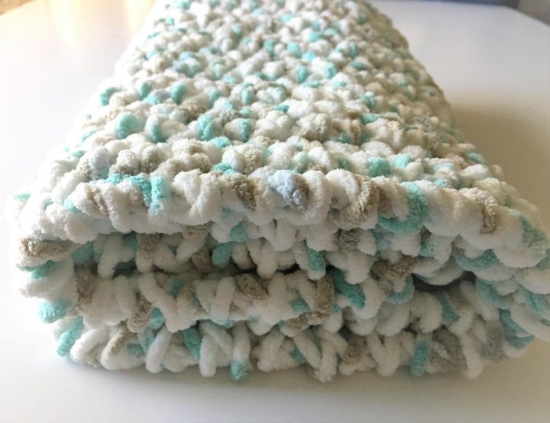 May include: A soft, crocheted baby blanket in white, beige, and light blue.