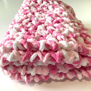 May include: A pink and white crocheted baby blanket with a soft, fluffy texture.