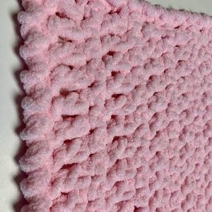 May include: A soft, pink crocheted baby blanket with a textured stitch pattern.
