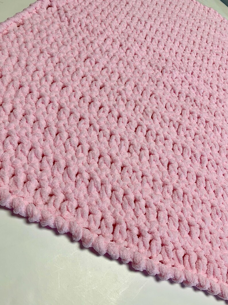 May include: A soft, pink crocheted blanket with a textured, fluffy surface.