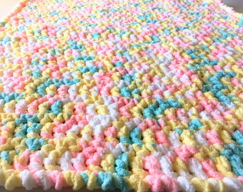 May include: A crocheted baby blanket in a pastel color scheme of pink, yellow, blue, and white.