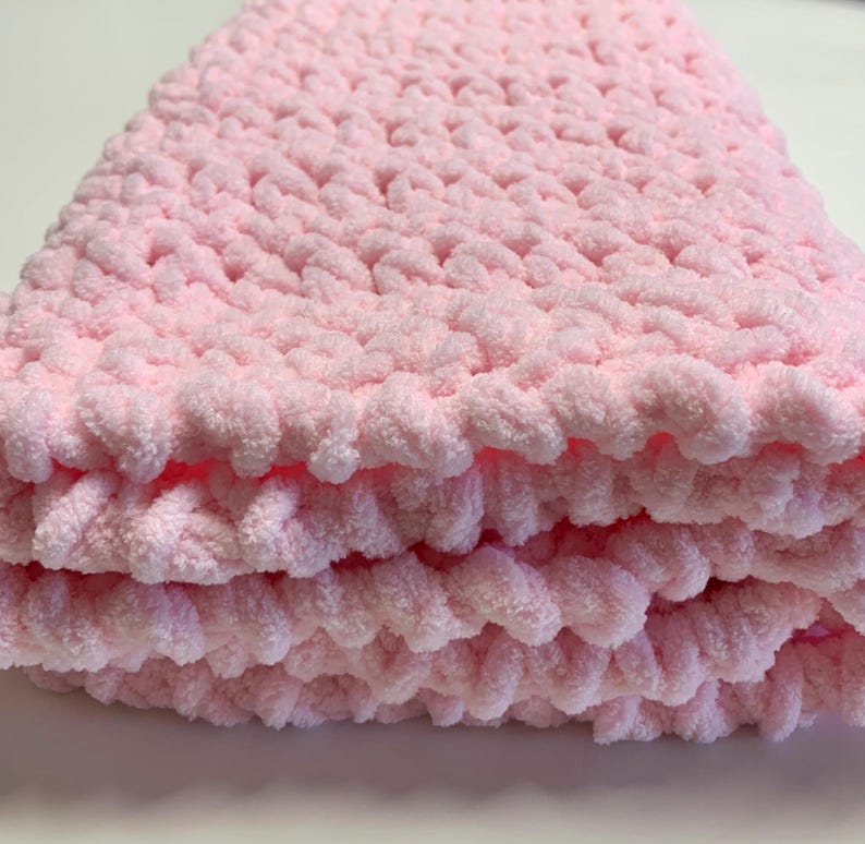 May include: A soft, pink crocheted baby blanket with a fluffy texture.
