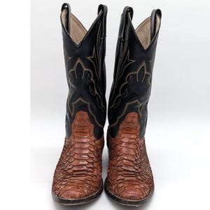 Könnte beinhalten: Ein Paar hohe Cowboystiefel mit einem strukturierten, braunen Fußteil aus Leder mit Schuppenmuster und einem Schaft aus glattem schwarzem Leder. Der schwarze obere Teil ist mit aufwendigen, hellen Ziernähten und Anziehschlaufen versehen.