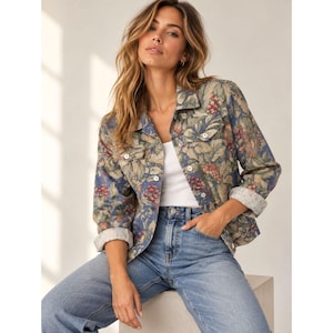 May include: A long-sleeved button-down jacket featuring a botanical print with blue, green, and red berry motifs. The jacket has a classic collar, two chest pockets with button closures, and white buttons. It is worn over a plain white tank top.