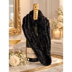 Puede incluir: Una bufanda infinita de piel sintética negra drapeada sobre una botella de champán Moët & Chandon. La botella presenta una etiqueta de cuello de papel de aluminio dorado con el texto MOËT y una etiqueta crema con el texto MOËT & CHANDON IMPÉRIAL.