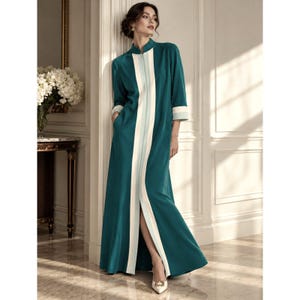 May include: A floor-length teal dress featuring a high collar, three-quarter length sleeves with light-colored cuffs, and a central vertical panel in white and light blue that runs down the front, creating a streamlined silhouette.