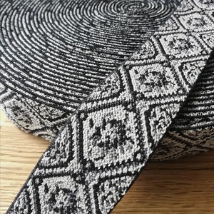 Könnte beinhalten: Schwarz-weißes elastisches Band mit geometrischem Muster. Das Band ist mit einem strukturierten, leicht erhabenen Design gewebt.