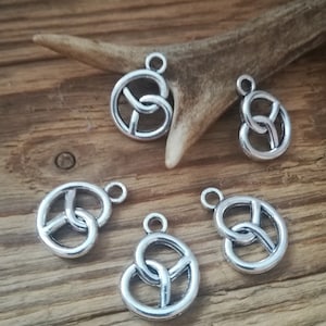 Könnte beinhalten: Fünf silberne Metallanhänger mit einem keltischen Knotendesign. Die Anhänger sind rund und haben oben ein Loch zum Anbringen an einer Halskette oder einem Armband.