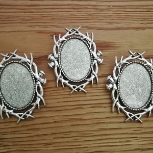 Könnte beinhalten: Drei silberfarbene ovale Metallrahmen mit einem Design aus Geweih um die Ränder. Die Rahmen sind leer und bereit für die Verwendung beim Basteln.