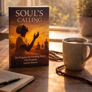 May include: A book titled "SOUL'S CALLING" with the subtitle "Ori Prayers for Finding One's Life Purpose" sits on a wooden table next to a mug of coffee and a string of beads. The book cover features an illustration of a person with arms raised.