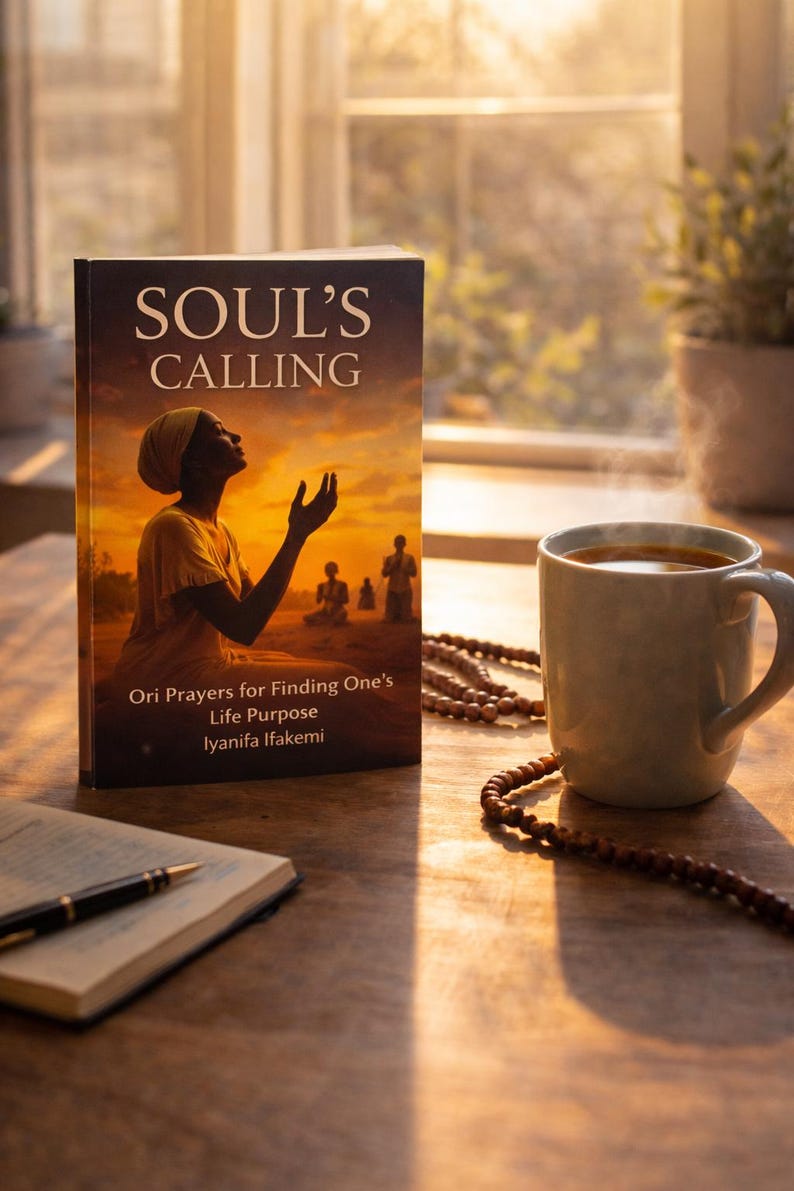 May include: A book titled "SOUL'S CALLING" with the subtitle "Ori Prayers for Finding One's Life Purpose" sits on a wooden table next to a mug of coffee and a string of beads. The book cover features an illustration of a person with arms raised.