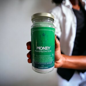 May include: A green and white palm wax candle with the text "MONEY MANIFESTATION" and a description of its purpose. The candle is 16 oz.