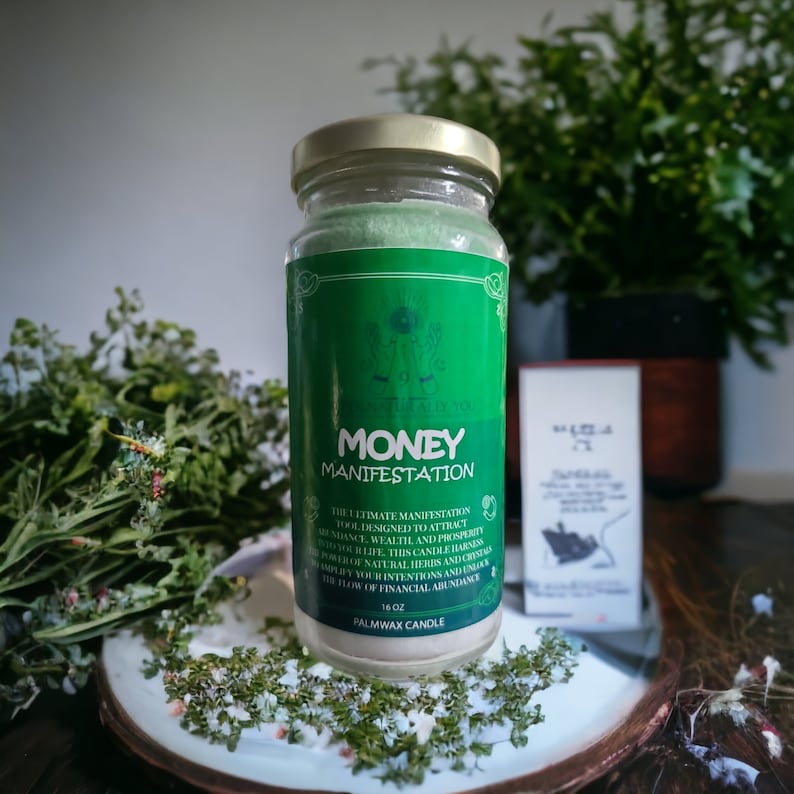 May include: A green glass jar candle with a gold lid. The label reads "NATURALLY YOU MONEY MANIFESTATION The ultimate manifestation tool designed to attract abundance, wealth and prosperity into your life. This candle harnesses the power of intentions and crystals to amplify your wealthers and unlock the flow of financial abundance. PALMWAX 16 OZ CANDLE"